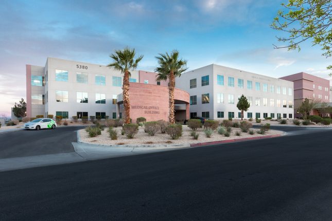 A medical office building at sunset with palm trees at the entrance and a road in the foreground.