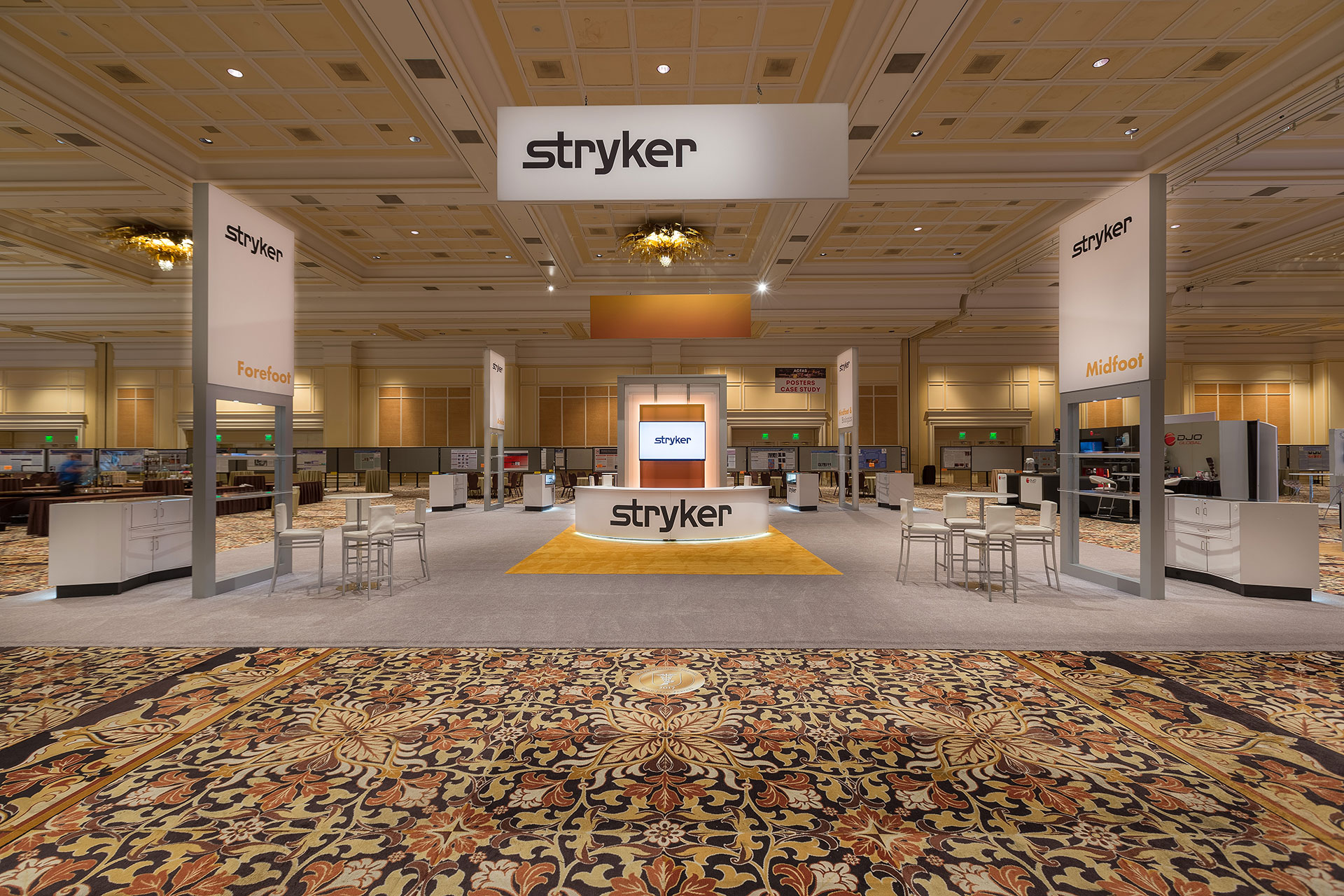 A centered photo of the Stryker booth at ACFAS 2017 with hanging banner, welcome counter with LCD screen, and four vertical signs all with the Stryker logo.
