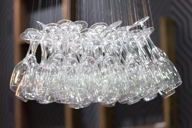 A close up of a chandelier made of suspended white wine glasses in front of a grey background.