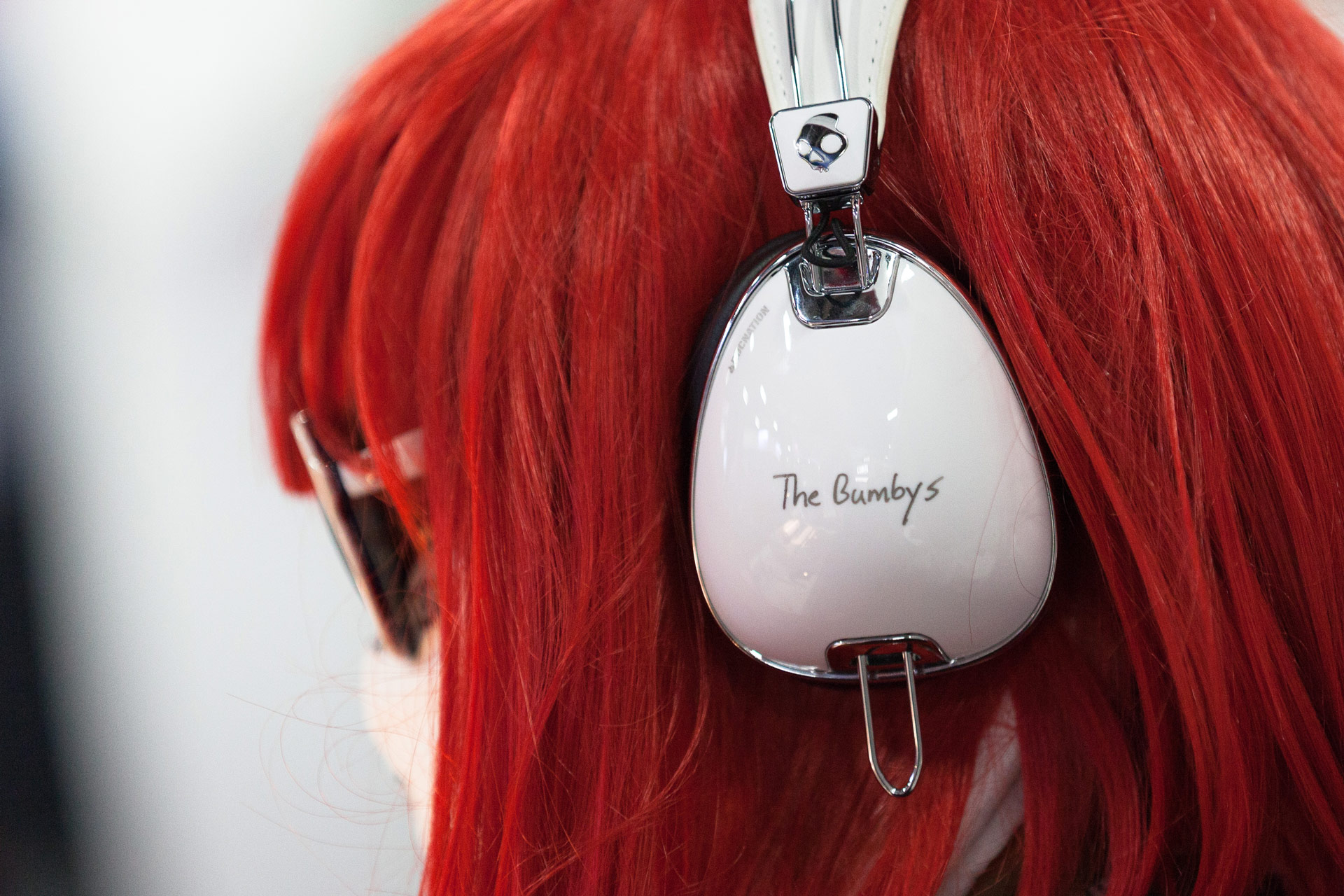 A side view of a red-haired woman with sunglasses and white headphones with "The Bumby's" written on the side.