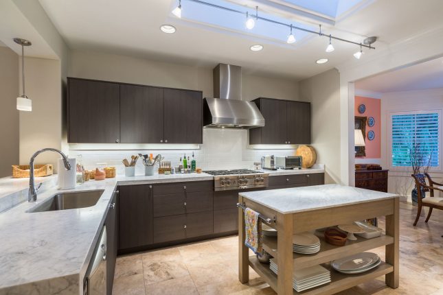 Modern kitchen with dark wood cabinets, white marble countertops and stainless steel hood and range with track lighting and skylight above.