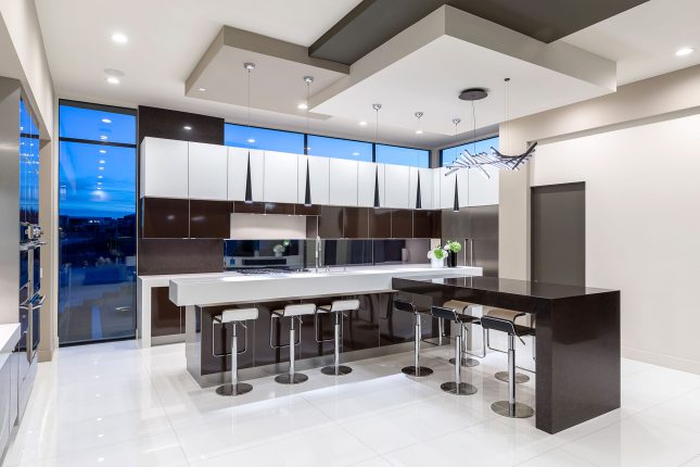 A kitchen with a white tile floor a white countertop, a dark brown coutnertop and glossy white and brown cabinets at dusk with blue in the windows.