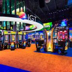 The IGT logo on a circular frame surrounding a video chandelier which hangs above slot machines at the IGT booth at G2E 2016