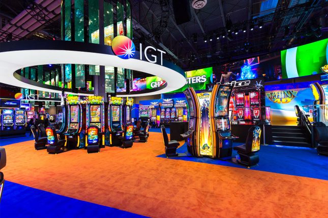 The IGT logo on a circular frame surrounding a video chandelier which hangs above slot machines at the IGT booth at G2E 2016