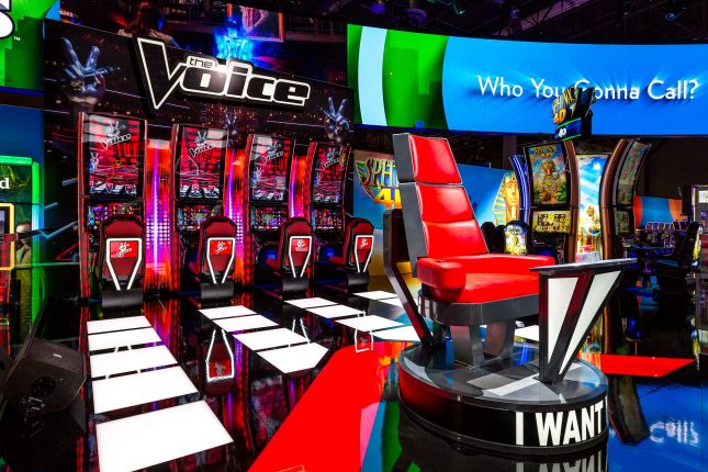 The red chair from The Voice in the foreground with The Voice slots in the background at the IGT booth at G2E 2016