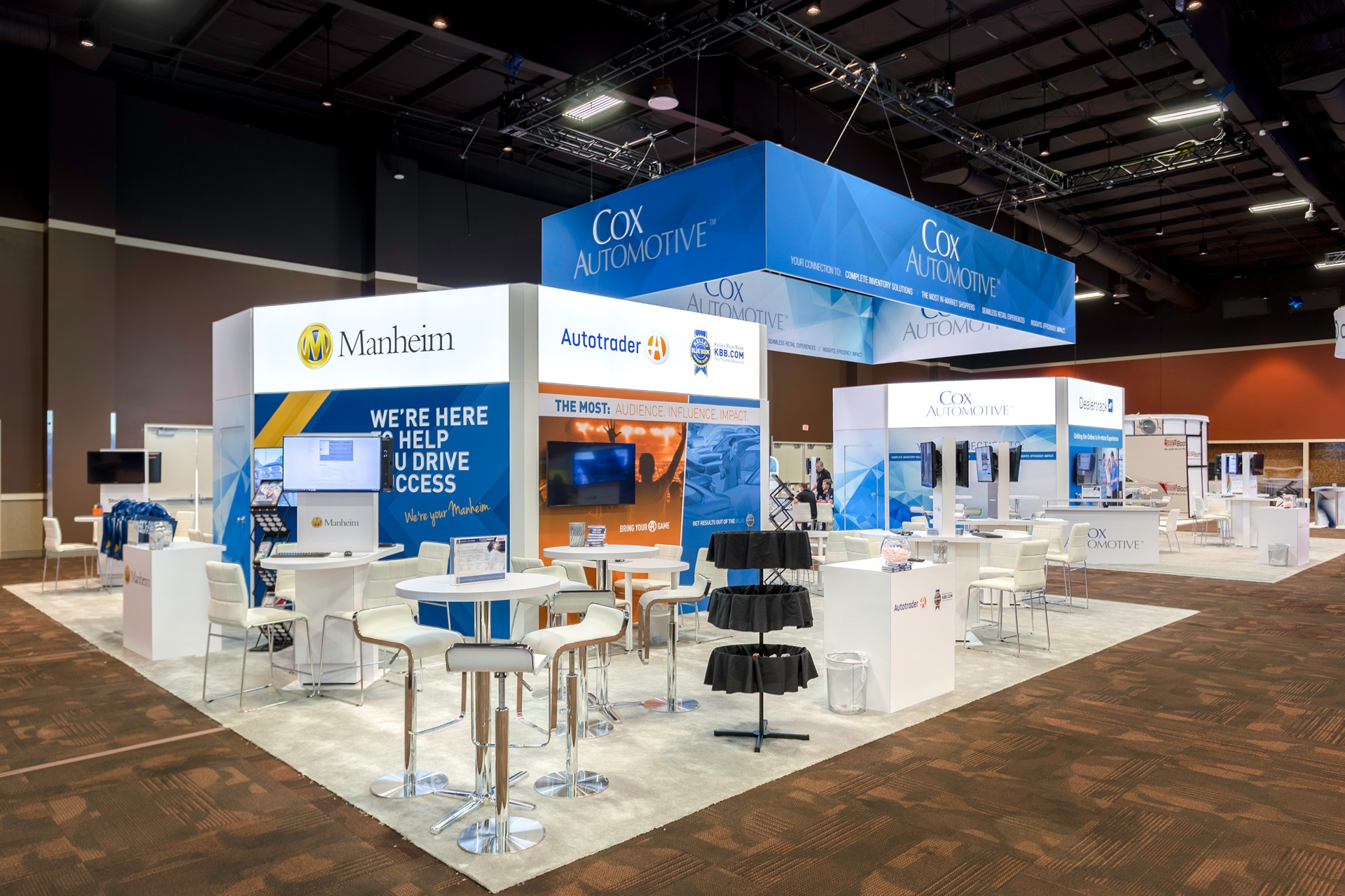 A blue and white trade show booth in multiple sections each with tall tables and chairs and a podium .