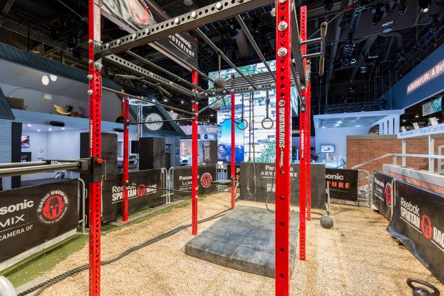Red and black slotted metal posts with gymnastic rings suspended inside a convention center.