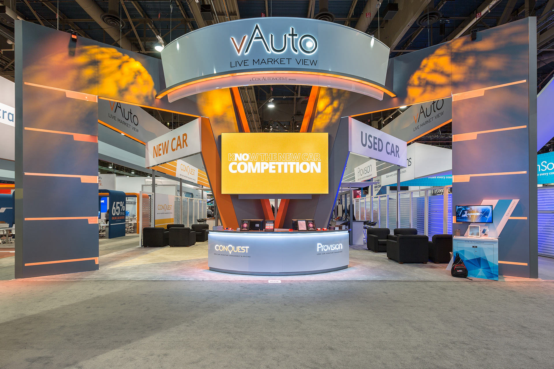 Grey and orange arch elements extending forward from a v-shaped centerpiece with a illunimated welcome counter and vAuto logo suspended above and an orange video screen directly center.