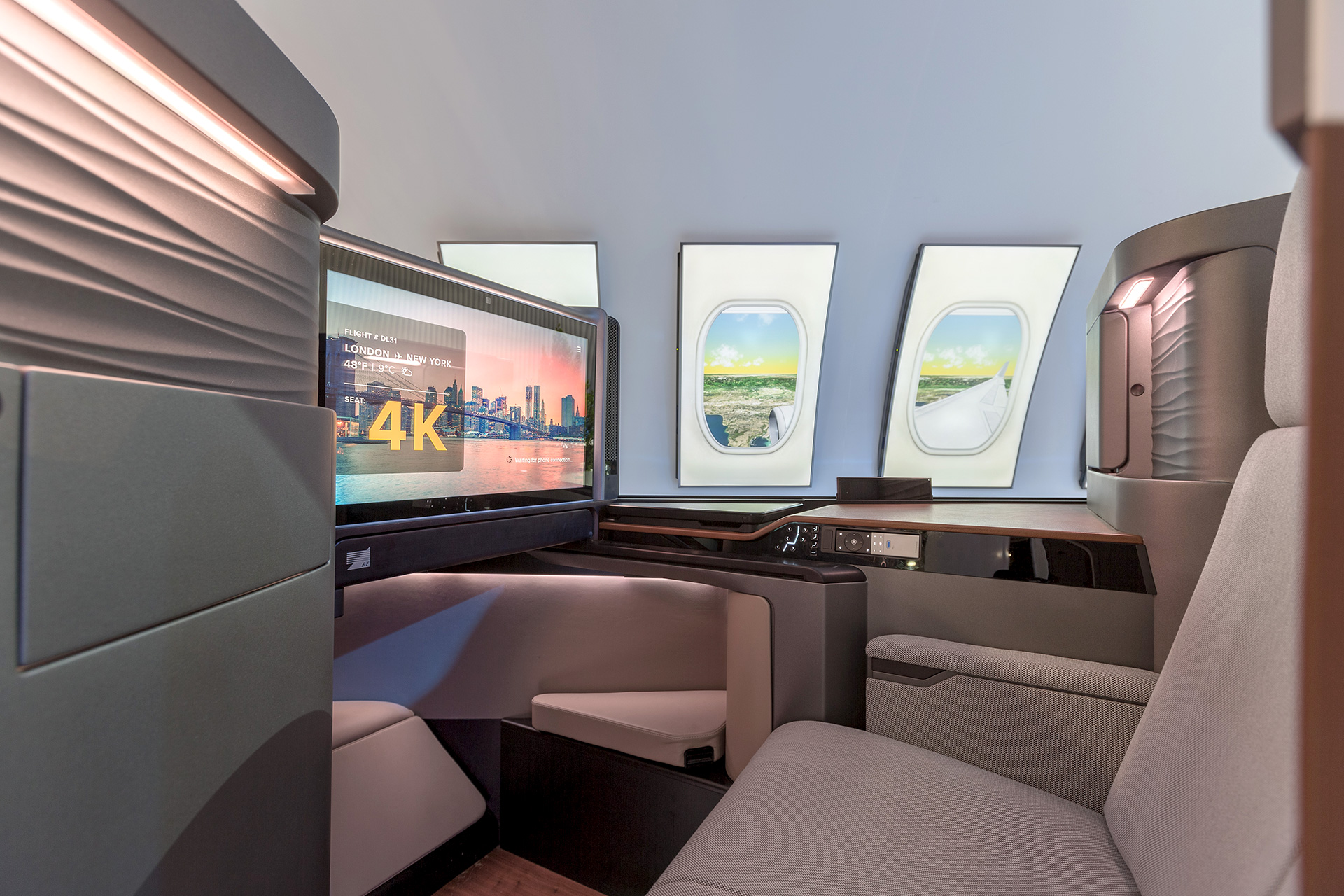A first-class airplane cabin exhibit with a beige fabric seat and video screen in the foreground an video screen emulating airplane windows in the background.