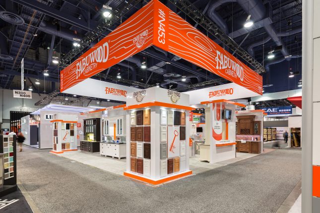 A vertical display of cabinet finishes in the foreground with multiple countertop and cabinet displays behind it all beneath a suspended sign which read "Fabuwood"