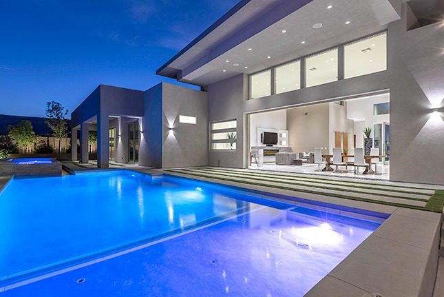 A backyard with a modern blue swimming pool and open wall to the interior of a modern home.