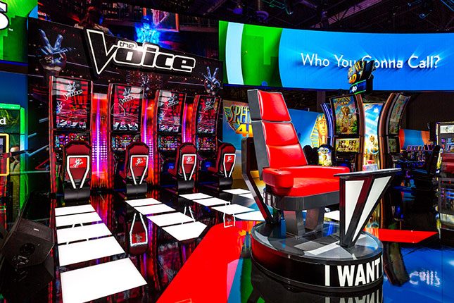 The red chair from The Voice in the foreground with The Voice slots in the background at the IGT booth at G2E 2016