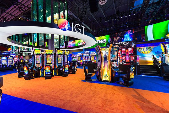 The IGT logo on a circular frame surrounding a video chandelier which hangs above slot machines at the IGT booth at G2E 2016