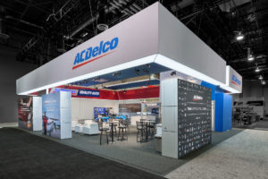 An angular view of the ACDelco tradeshow booth with a suspended grey banner and graphic blocks as walls with barstools, tables, and displays inside.
