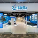 The exterior of the Oddello shop with glass walls and glass sliding doors and a white and blue interior with beds on display.