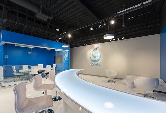 A white illuminated countertop with white barstools and a blue conference room with glass walls in the background as well as an Oddello logo on the back wall.