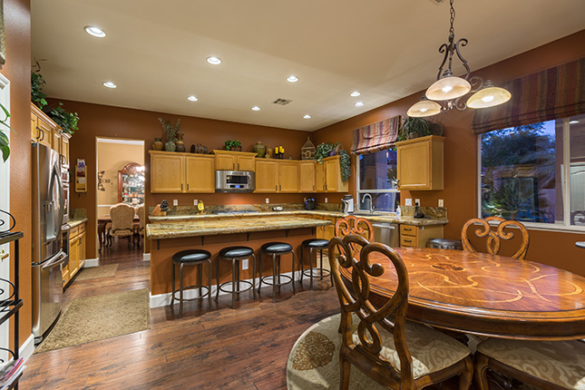 A kitchen with dark hardwood floors, a round wooden table in the foreground and a granite island and oak cabinets in the background.