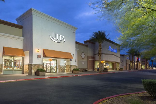 A shopping complex at dusk with a white Ulta store in the foreground and beige Marshalls beside it and other retailers in the distance.