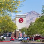 The off-white tower of a target retail store with red bulls-eye logo atop surrounded by trees with yellow blossoms and a desert mountain the background