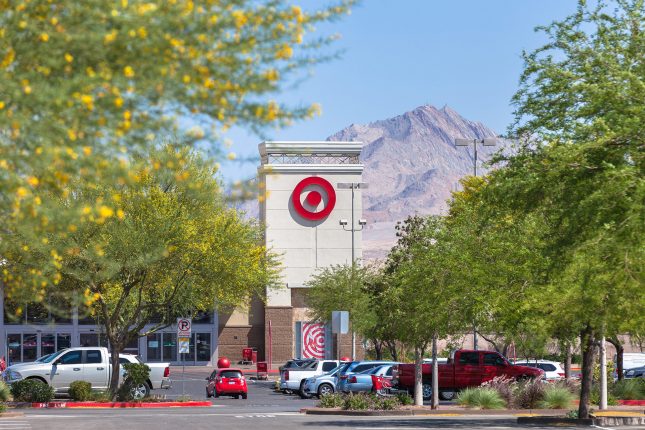 The off-white tower of a target retail store with red bulls-eye logo atop surrounded by trees with yellow blossoms and a desert mountain the background