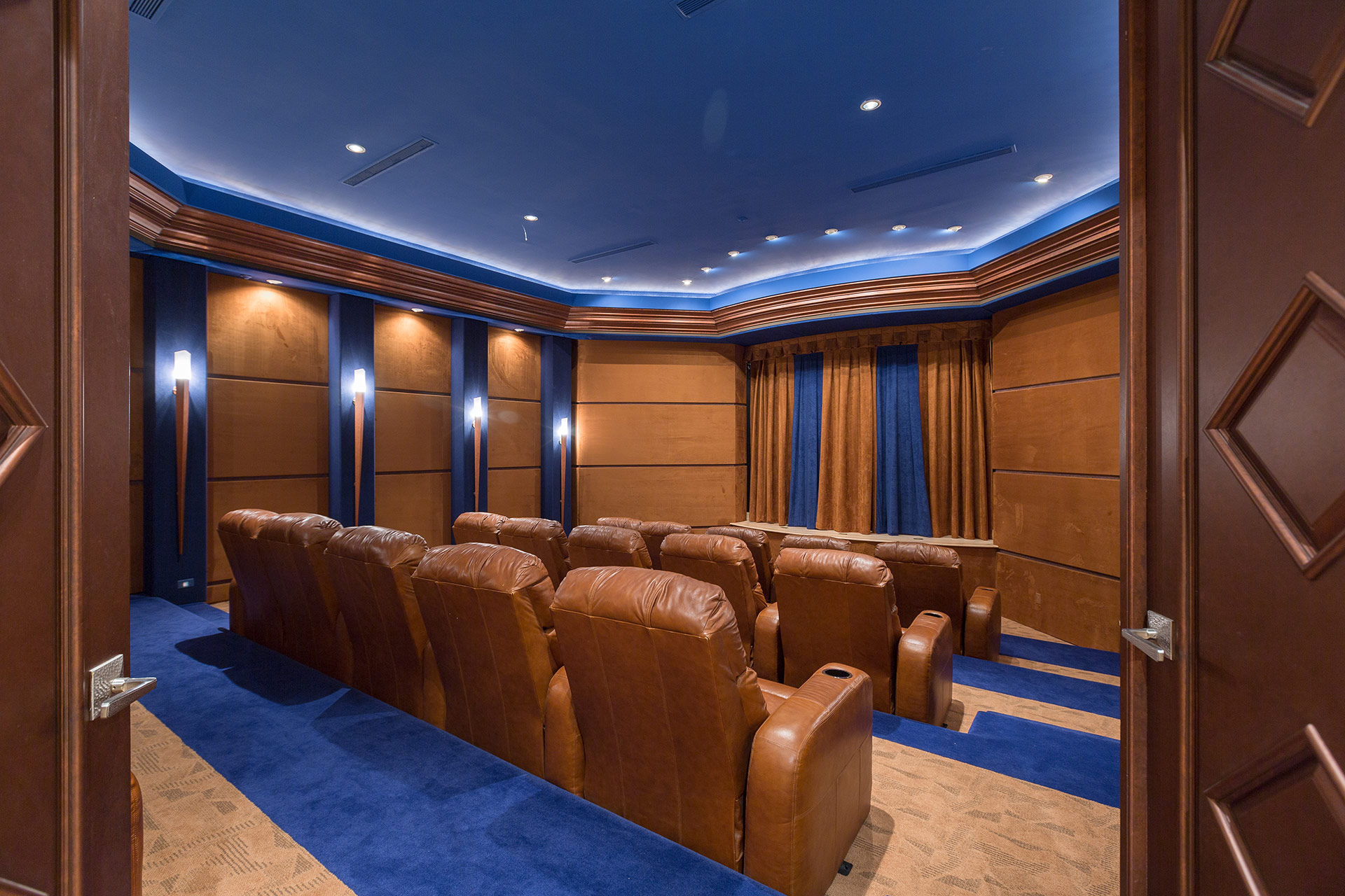 Double doors opening to a home theater with brown recliners, blue ceiling, blue and tan carpet and a blue a brown curtain covering the screen.