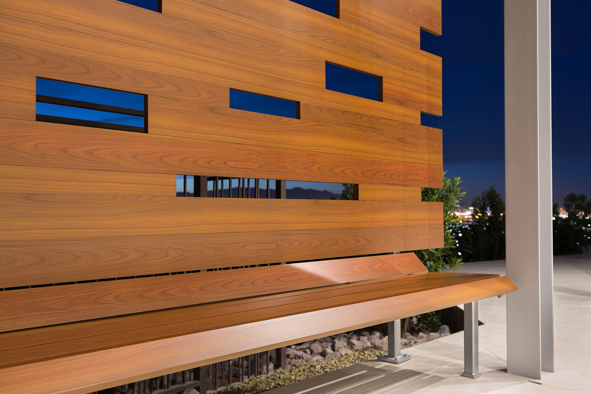 A wood-like aluminum backyard bench on a light beige tiled patio with Las Vegas city lights in the background.