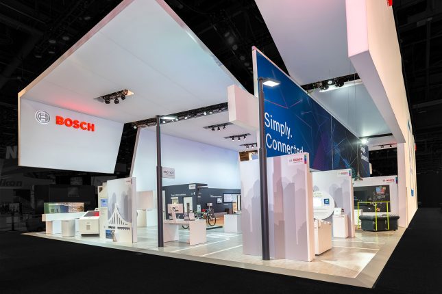 A large Bosch tradeshow exhibit made of suspended white panels and multiple kiosks with the red Bosch logo on the top left.