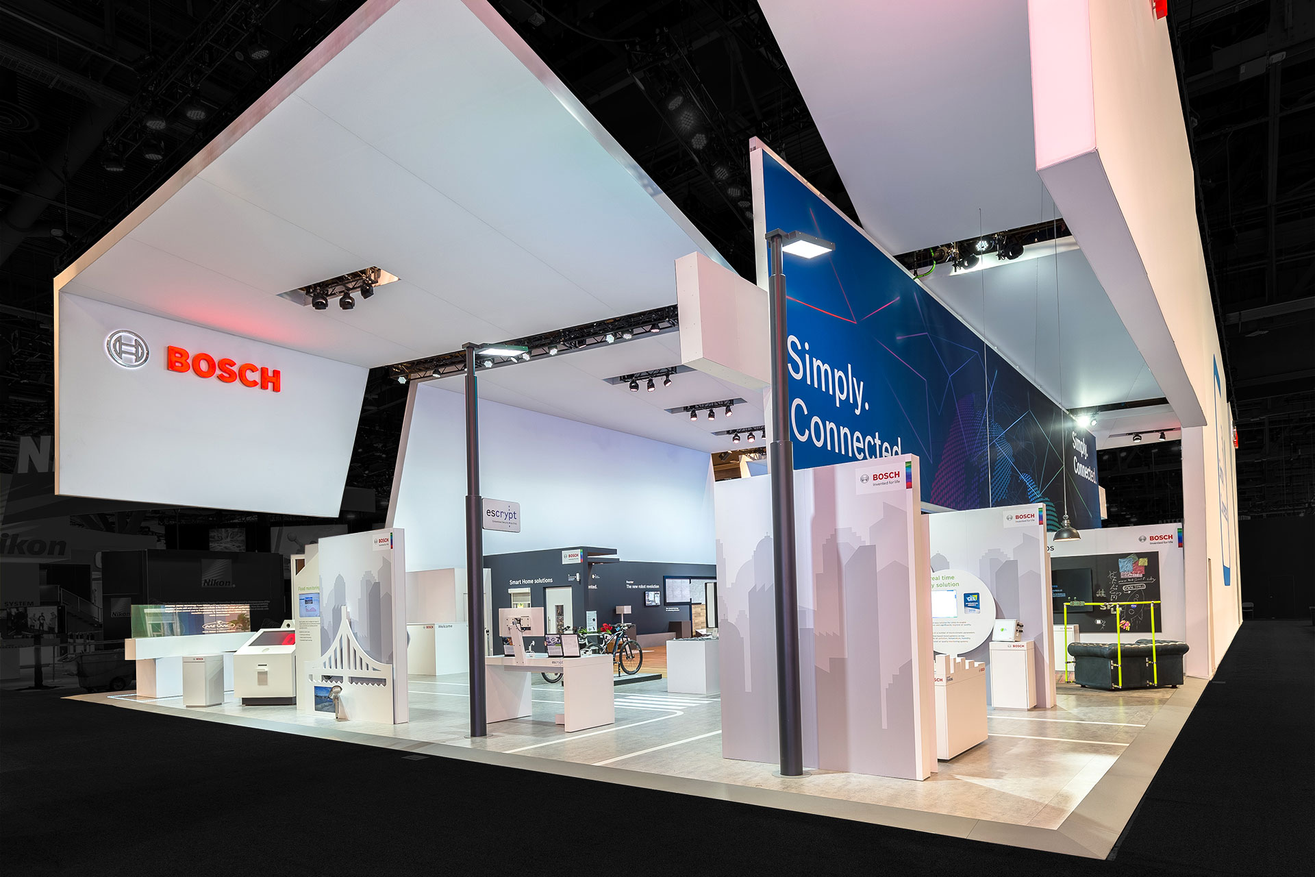 A large Bosch tradeshow exhibit made of suspended white panels and multiple kiosks with the red Bosch logo on the top left.