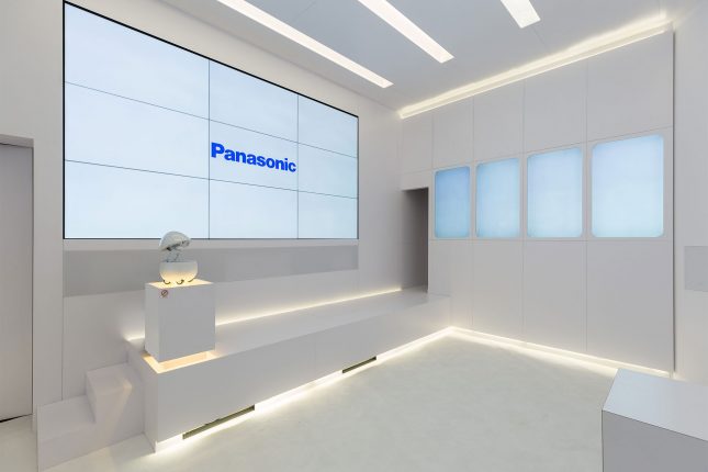 A white room with a nine-panel video wall with the Panasonic logo displayed in blue and on the right four frosted widows with rounded corners.