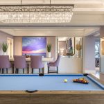 Custom Las Vegas Guest Suite with a Blue Pool table in the foreground, lavender-colored bartools surrounding a bar behind and a wide crystal chandelier above.