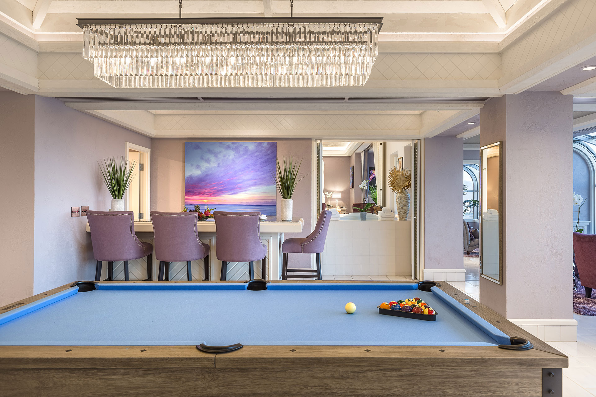 Custom Las Vegas Guest Suite with a Blue Pool table in the foreground, lavender-colored bartools surrounding a bar behind and a wide crystal chandelier above.