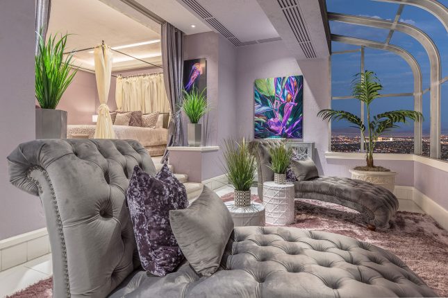 Two grey, pin-cushioned velvet setees in hotel room facing the windows with a twilight sky in the distance.