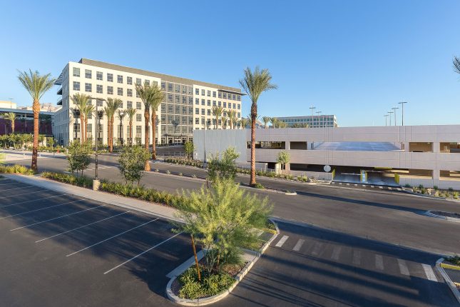 A six-story office building and adjacent three-story parking structure in daytime with streets and landscaping in the foreground.