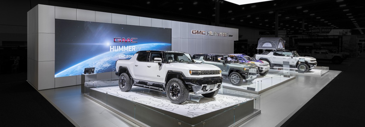 Four electric vehicles at the 2021 SEMA Hummer EV Exhibit at West Hall in Las Vegas Convention Center. The background is darkened highlighting the exhibit.