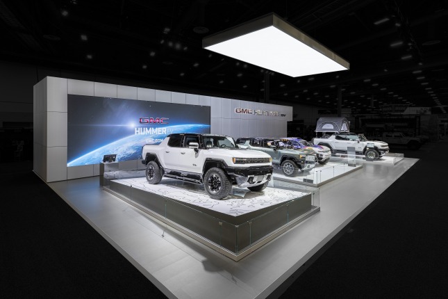 Four electric vehicles at the 2021 SEMA Hummer EV Exhibit at West Hall in Las Vegas Convention Center. The background is darkened highlighting the exhibit.