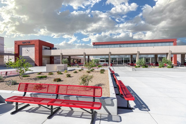 A technical high school exterior with red benches in the foreground raised planters with desert landscape behind and a wide two-story building in the background.